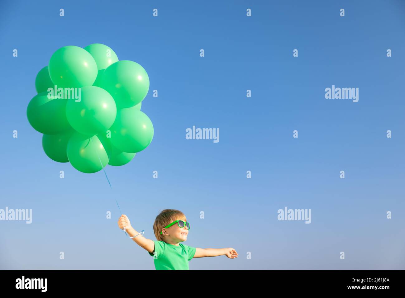 Glückliches Kind spielt mit leuchtend grünen Luftballons im Freien. Kind mit Spaß gegen blauen Sommerhimmel Hintergrund. Ökologie und aktives Lifestyle-Konzept Stockfoto