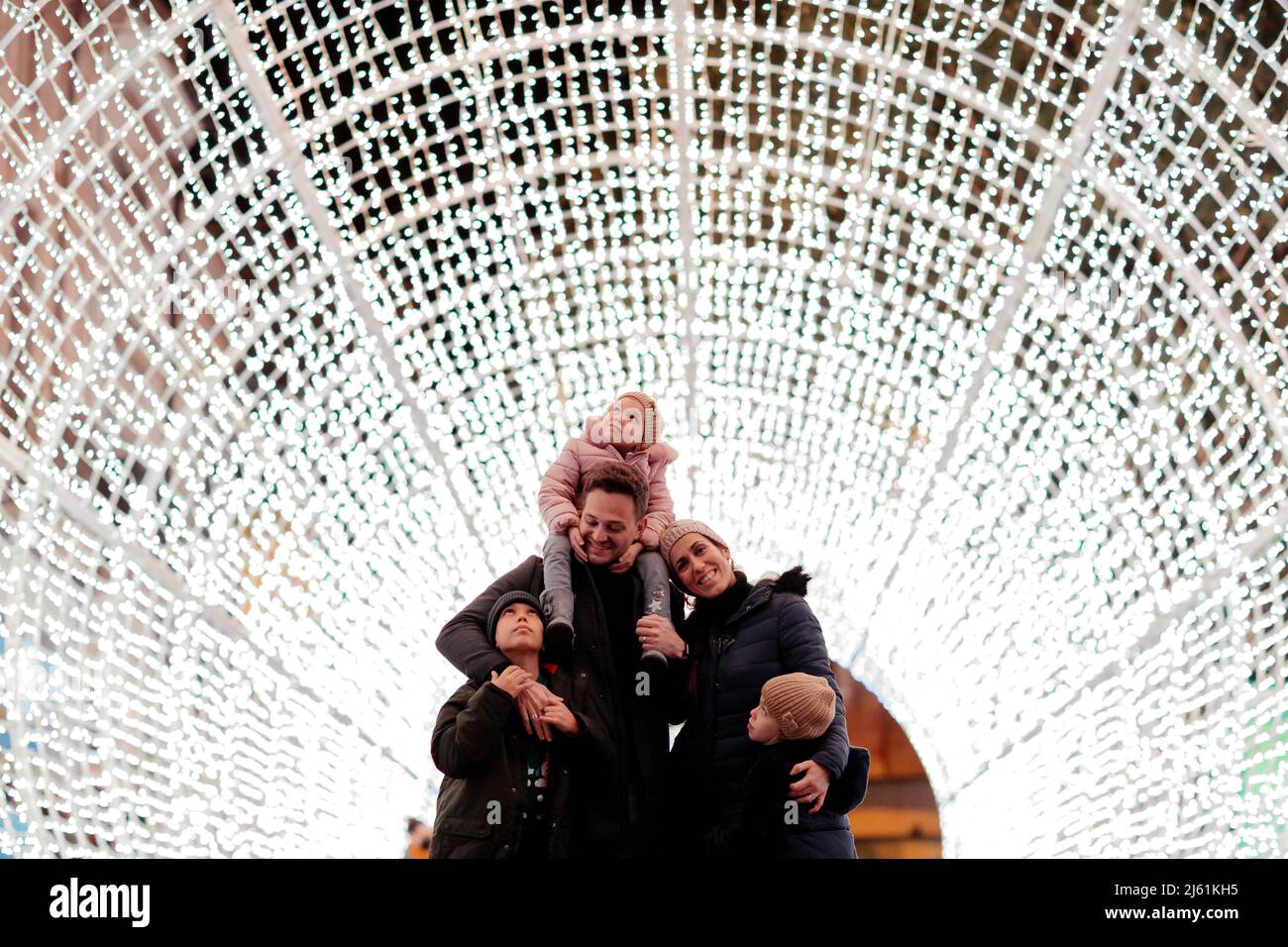Glücklicher Vater, der seine Tochter auf den Schultern trägt und mit seiner Familie im beleuchteten Tunnel steht Stockfoto