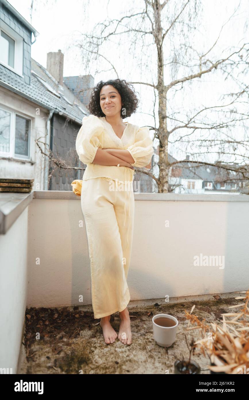 Lächelnde Frau mit gekreuzten Armen, die auf dem Balkon stehen Stockfoto