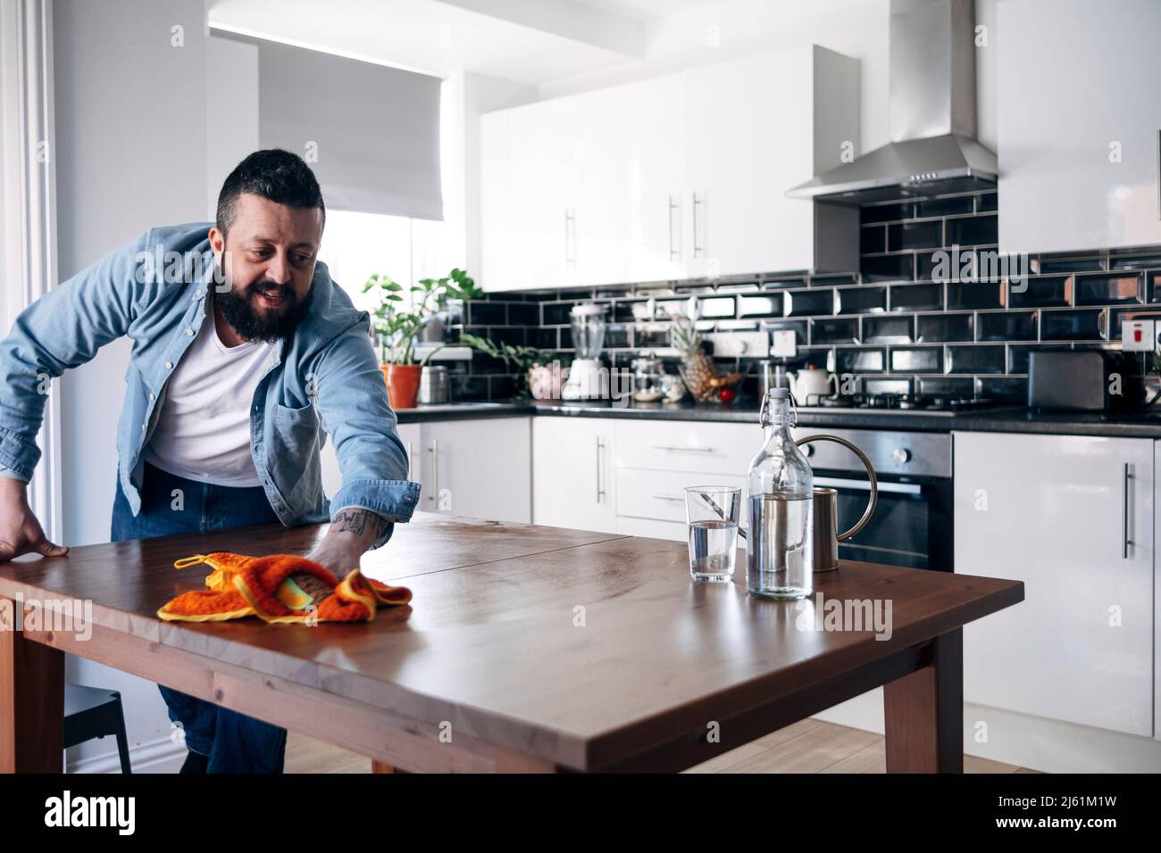 Mann, der die Kücheninsel mit Tuch in der Küche zu Hause putzt Stockfoto