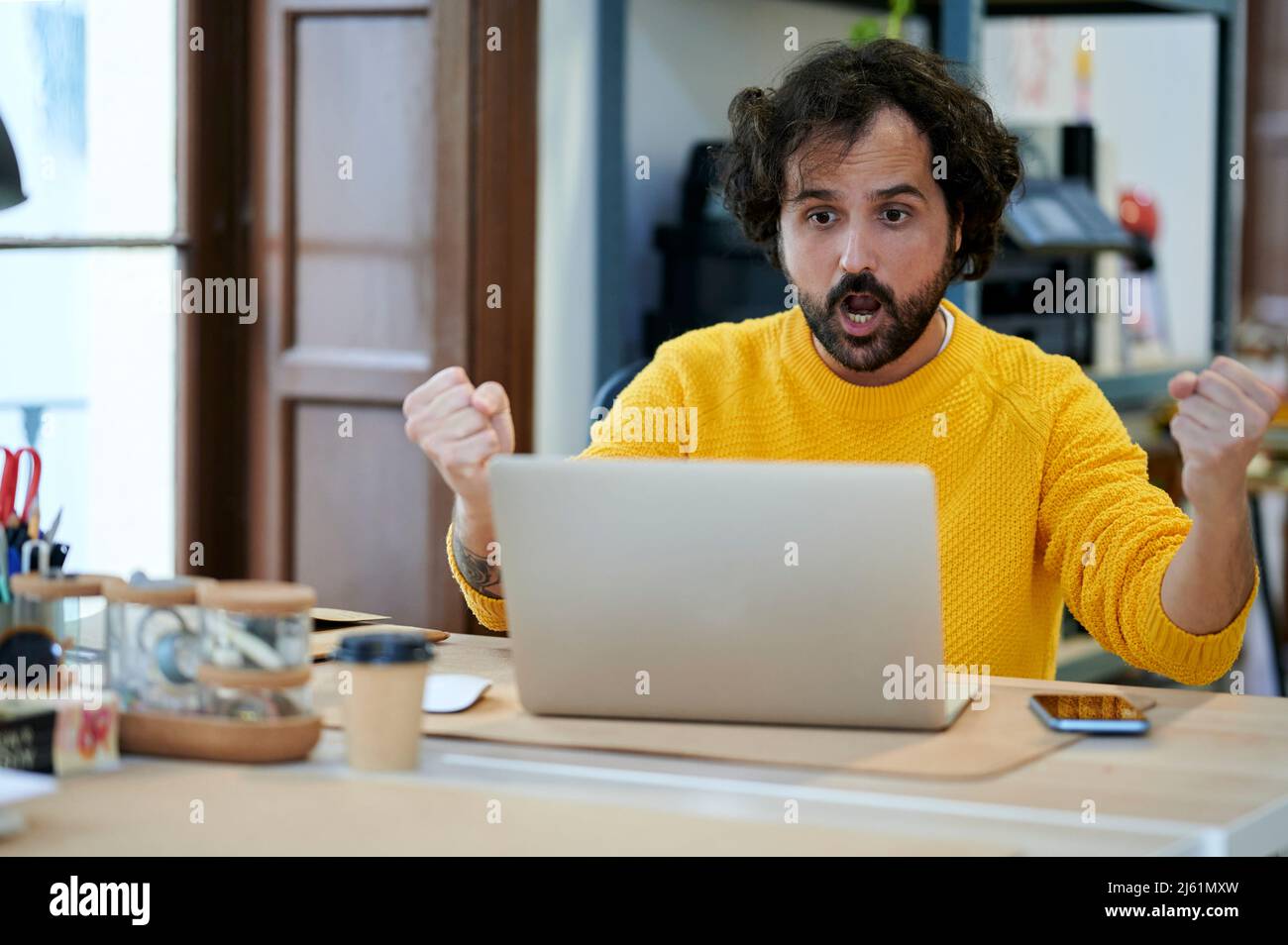 Begeisterter Geschäftsmann mit Laptop, der Erfolg durch gestikulierte Triumph im Büro zum Ausdruck bringt Stockfoto