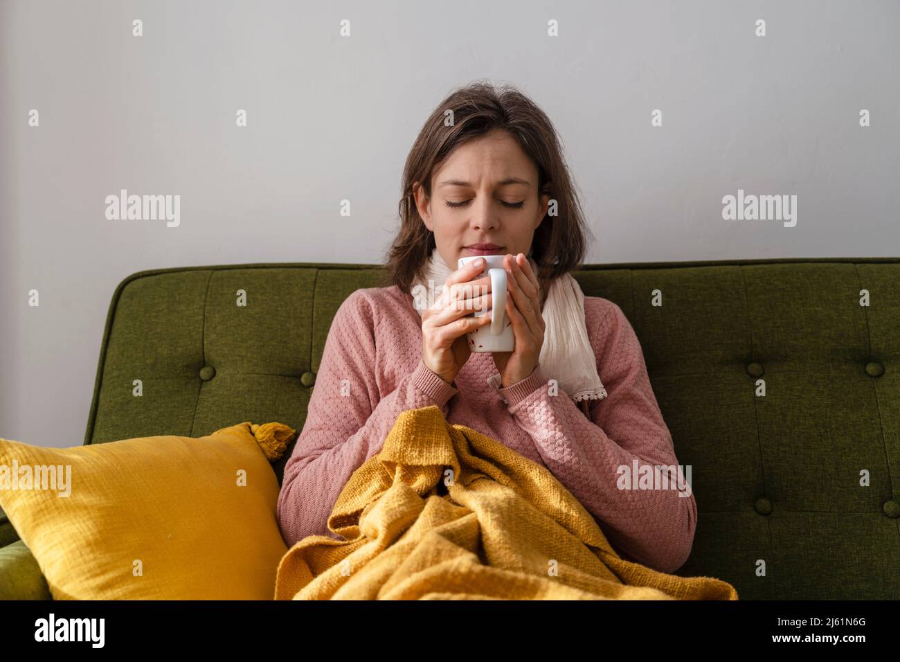 Kranke Frau mit Teetasse, die zu Hause auf dem Sofa sitzt Stockfoto