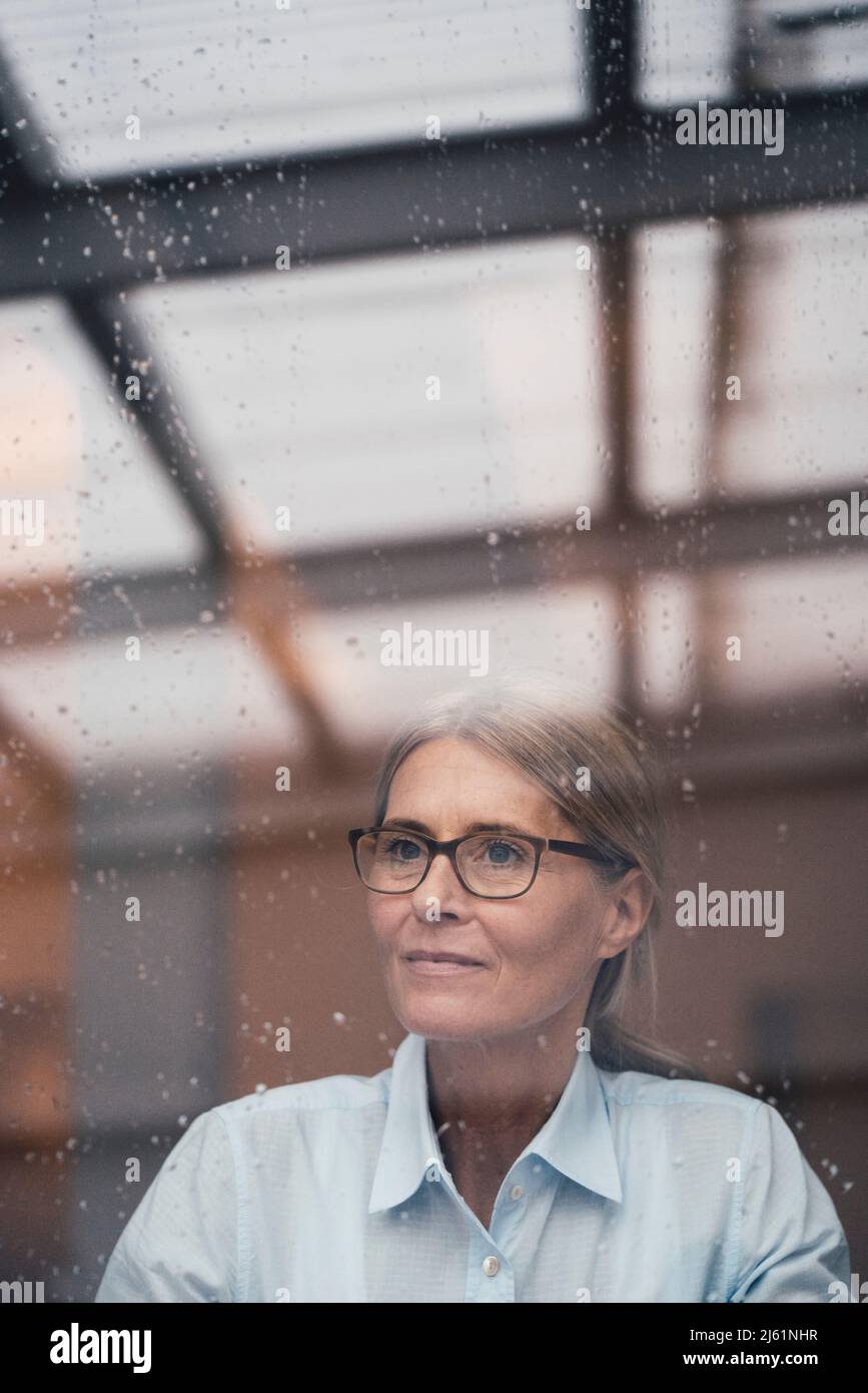 Eine durchdachte Geschäftsfrau, die durch ein Glas Arbeitsplatz gesehen wird Stockfoto