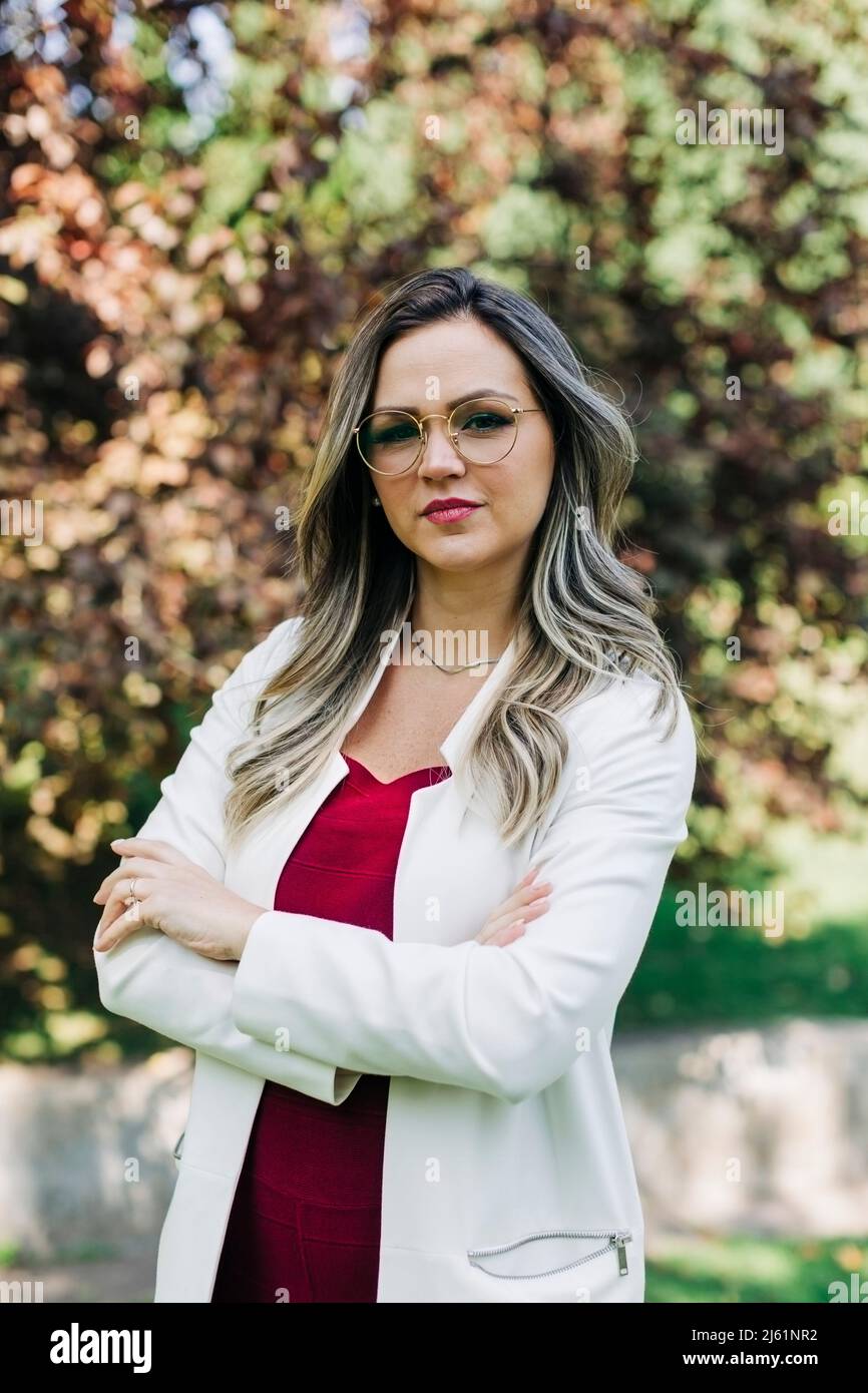 Selbstbewusste Geschäftsfrau, die mit gekreuzten Armen im Park steht Stockfoto