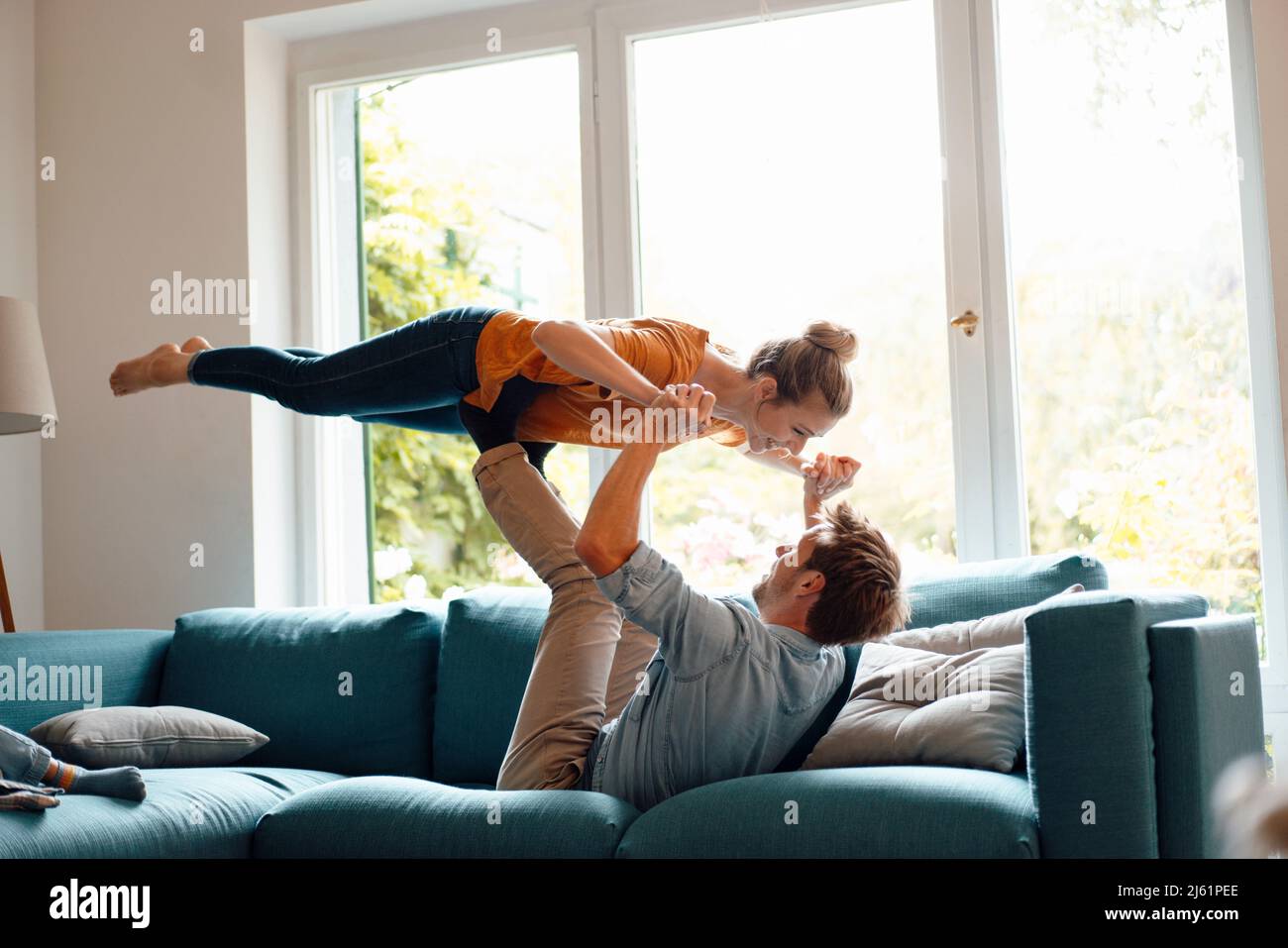 Mann, der Frau auf den Beinen auf dem Sofa im Wohnzimmer zu Hause liegend hebt Stockfoto