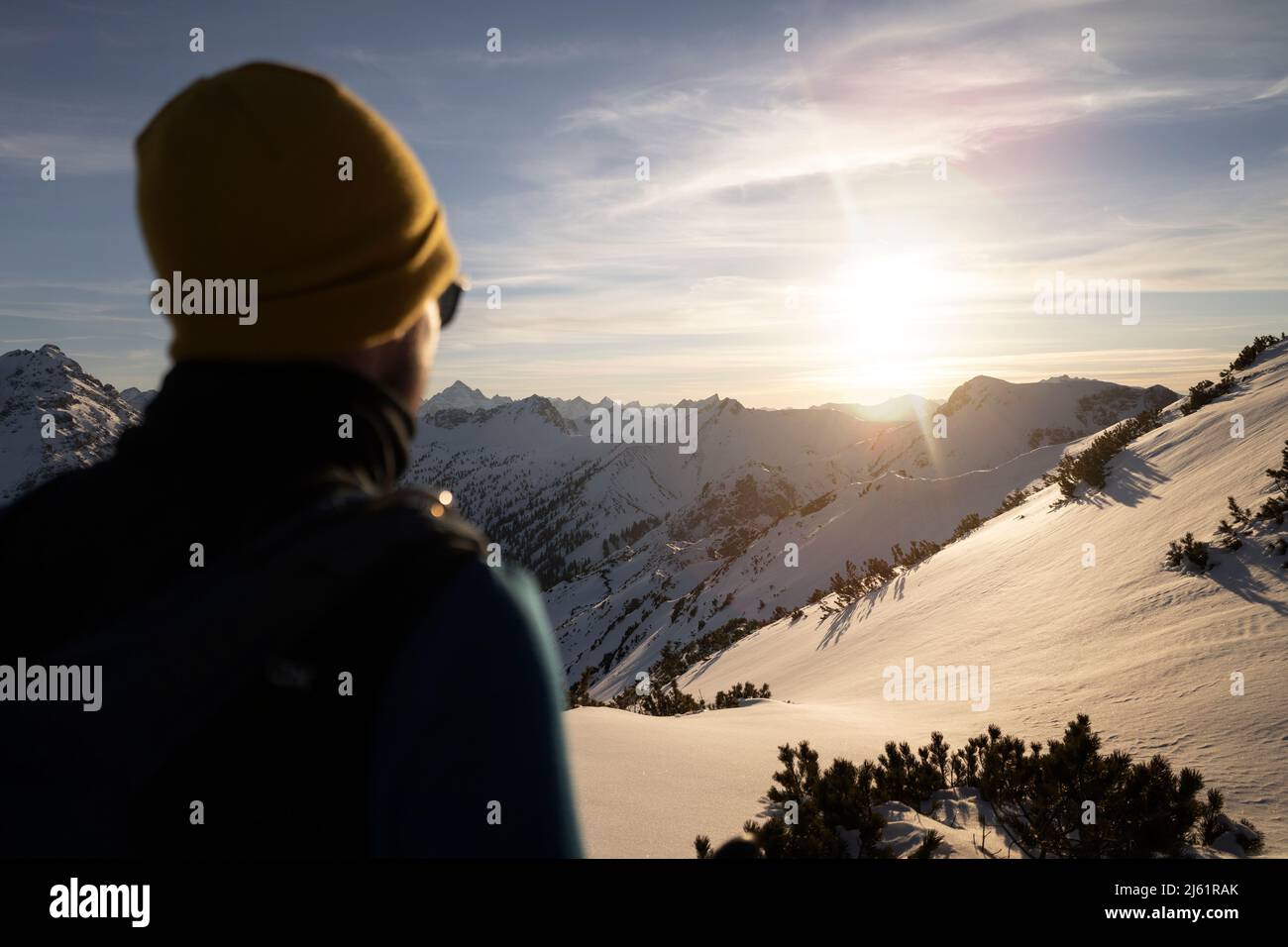 Mann mit Strickmütze, der den Sonnenaufgang auf dem verschneiten Berg genießt Stockfoto