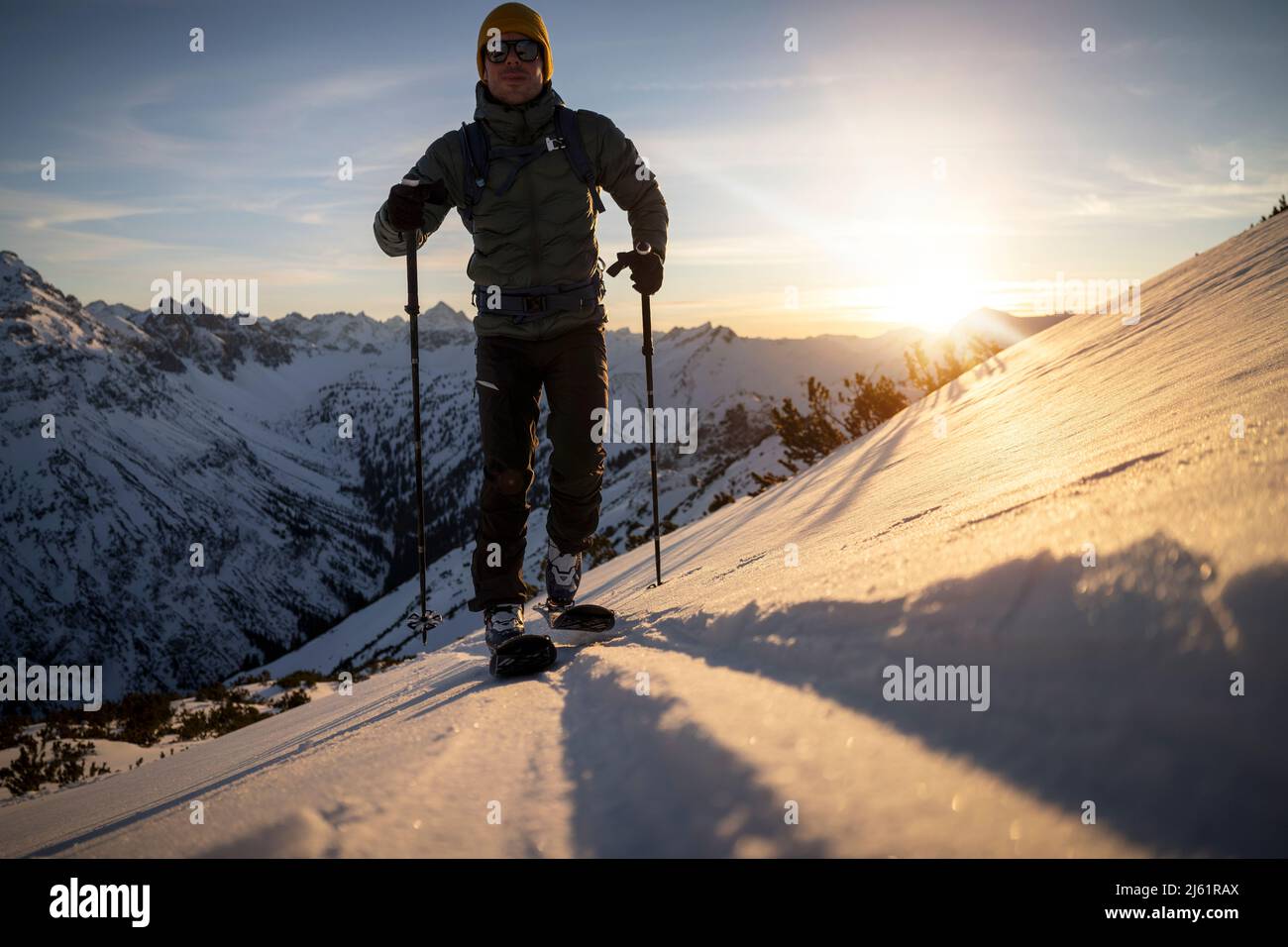 Mann mit Skistock, der bei Sonnenaufgang auf einem schneebedeckten Berg läuft Stockfoto