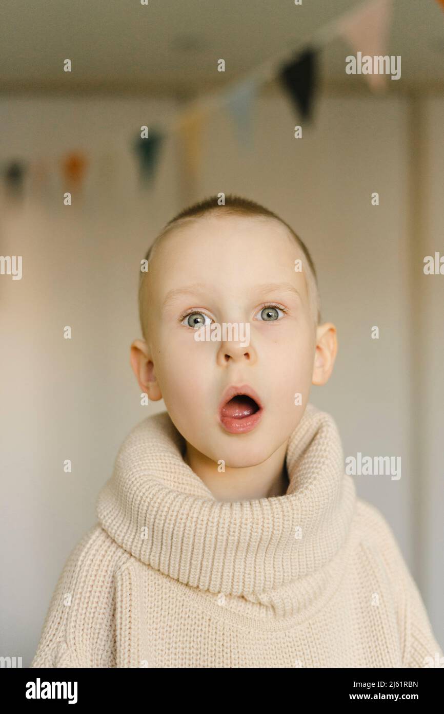Überrascht Junge mit Mund offen in Rollkragenpullover zu Hause Stockfoto