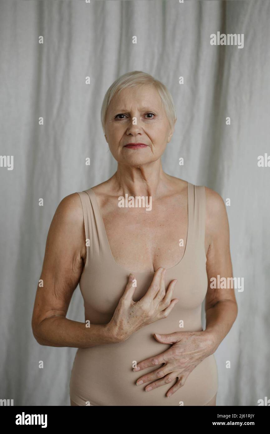 Ältere Frau im Body, die zu Hause vor dem Vorhang steht Stockfoto