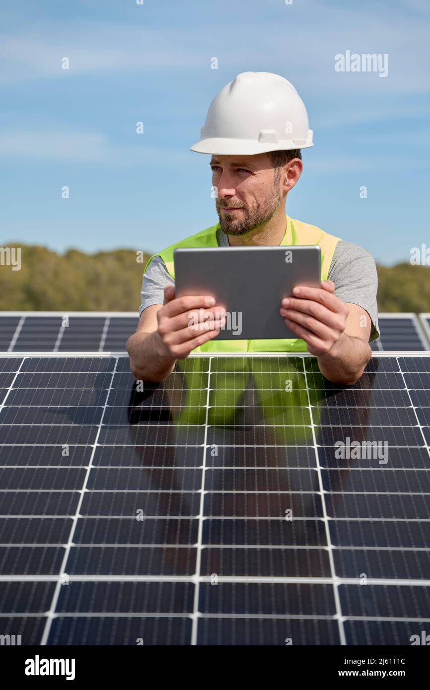 Techniker mit Hardhut und Tablet-PC zwischen Solarmodulen auf dem Dach Stockfoto