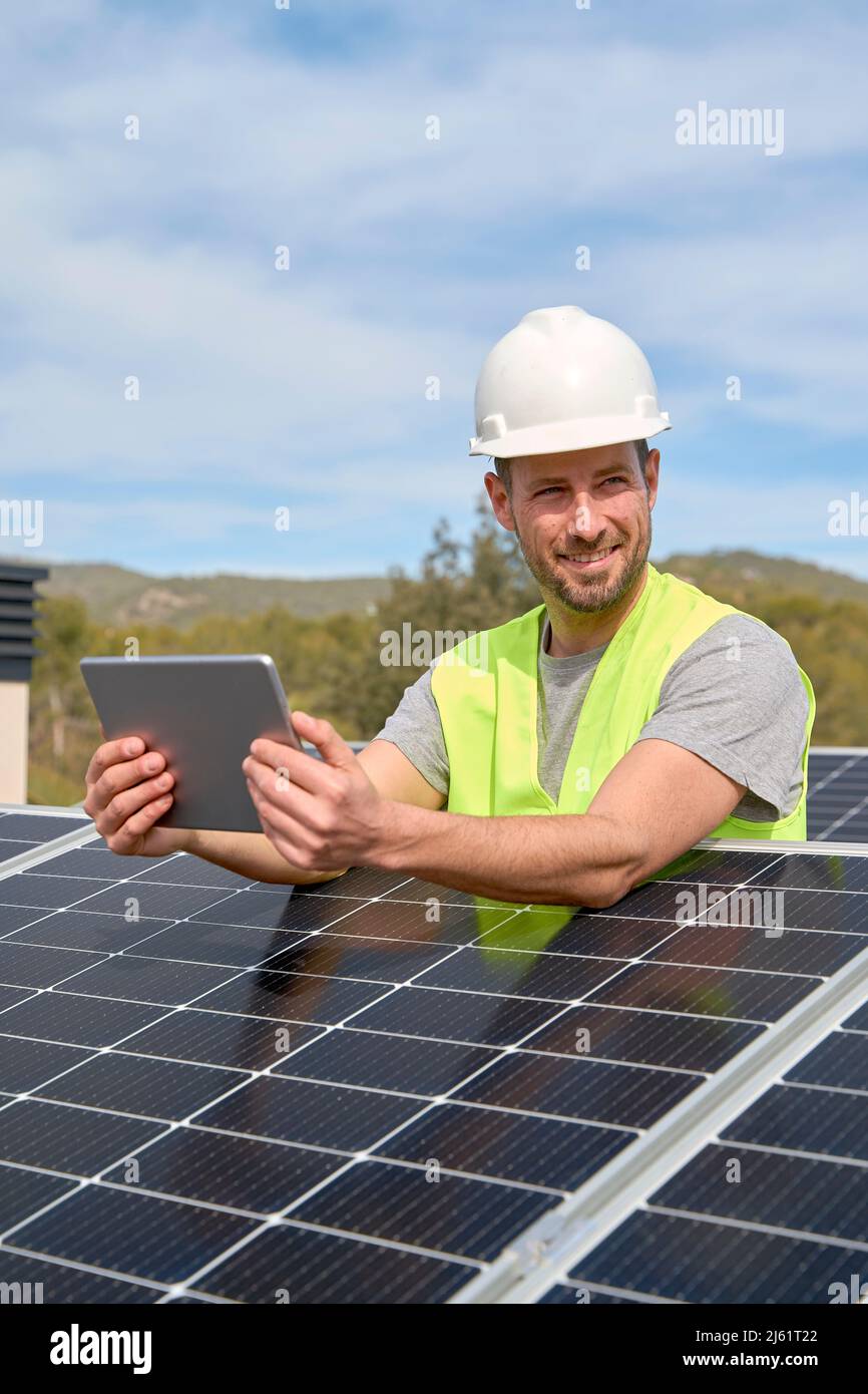 Lächelnder Ingenieur mit Tablet-PC zwischen Solarzellen auf dem Dach Stockfoto
