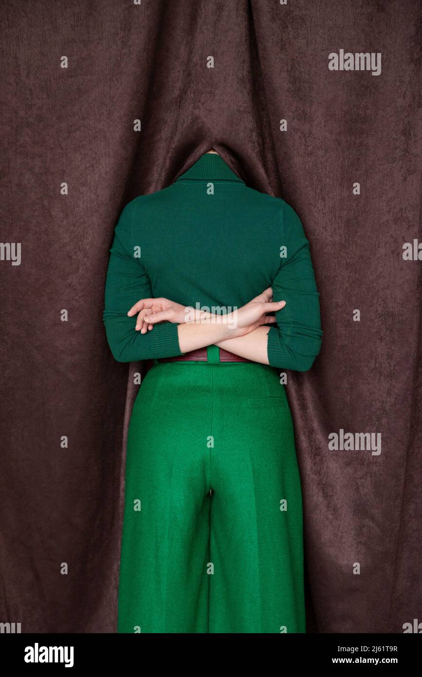 Frau mit hinter dem Rücken gekreuzten Armen, die den Kopf im Vorhang versteckt Stockfoto