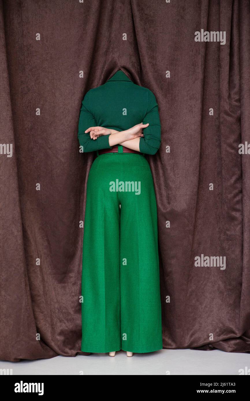 Junge Frau, die mit hinter dem Rücken gekreuzten Armen steht und den Kopf im Vorhang versteckt Stockfoto