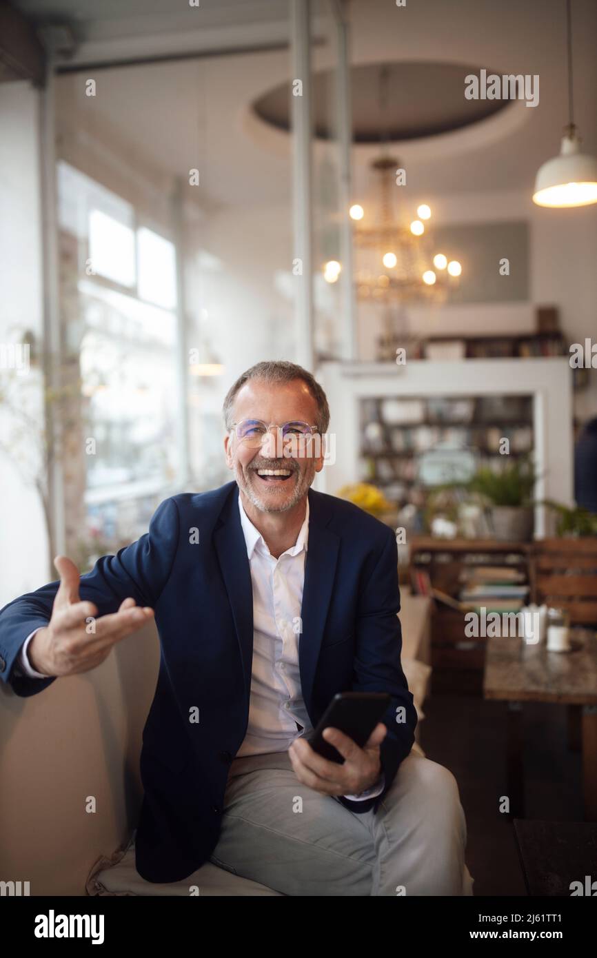 Fröhlicher Geschäftsmann mit Smartphone gestikuliert mit der Hand Stockfoto
