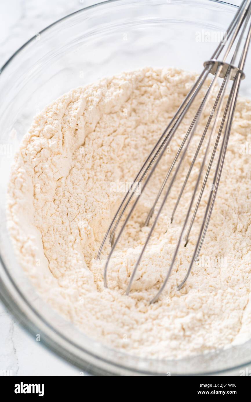 Zitronenkeks mit weißer Schokolade. Mischen Sie trockene Zutaten mit einem Handbesen in einer großen Glasschüssel, um Zitronenplätzchen mit weißer Schokolade zu backen. Stockfoto