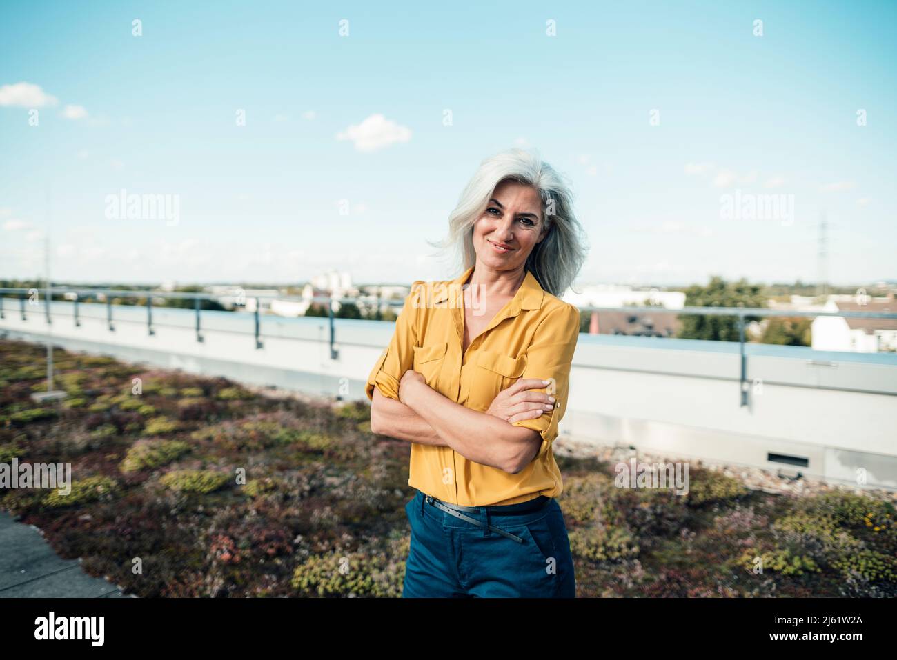 Lächelnde Geschäftsfrau, die mit gekreuzten Armen im Büropark steht Stockfoto