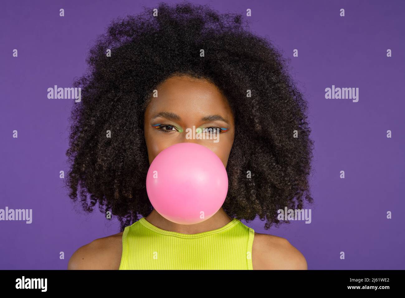 Schöne junge Frau bläst rosa Kaugummi vor lila Hintergrund Stockfoto