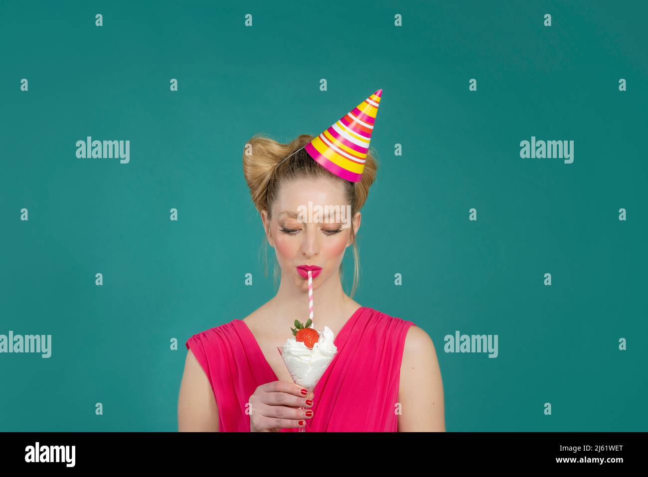 Junge Frau im Partyhut mit Trinkcreme und Erdbeercocktail mit Stroh vor grünem Hintergrund Stockfoto