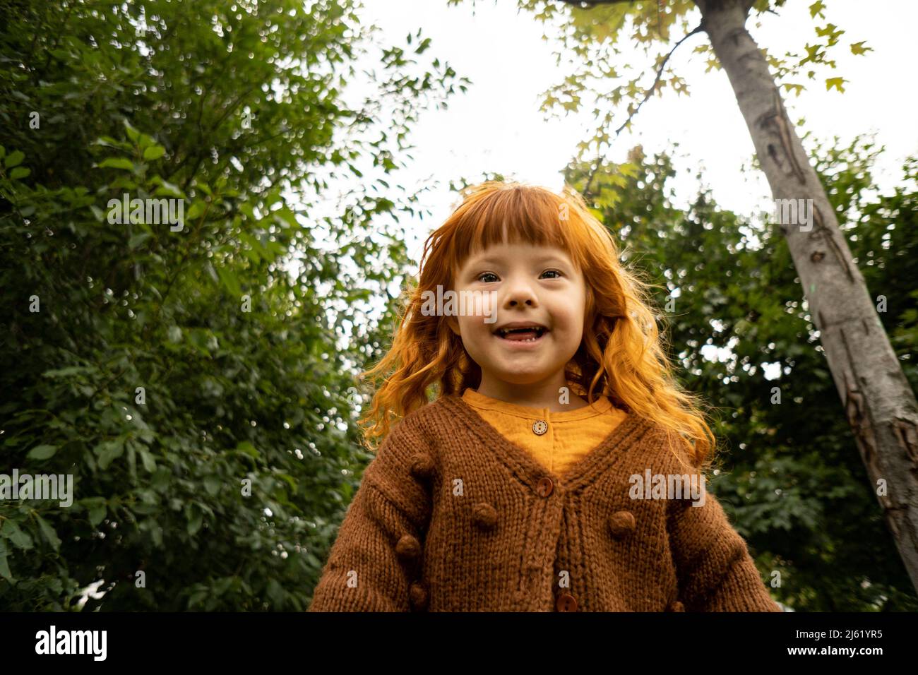 Lächelndes Mädchen mit Down-Syndrom, das vor Bäumen im öffentlichen Park steht Stockfoto