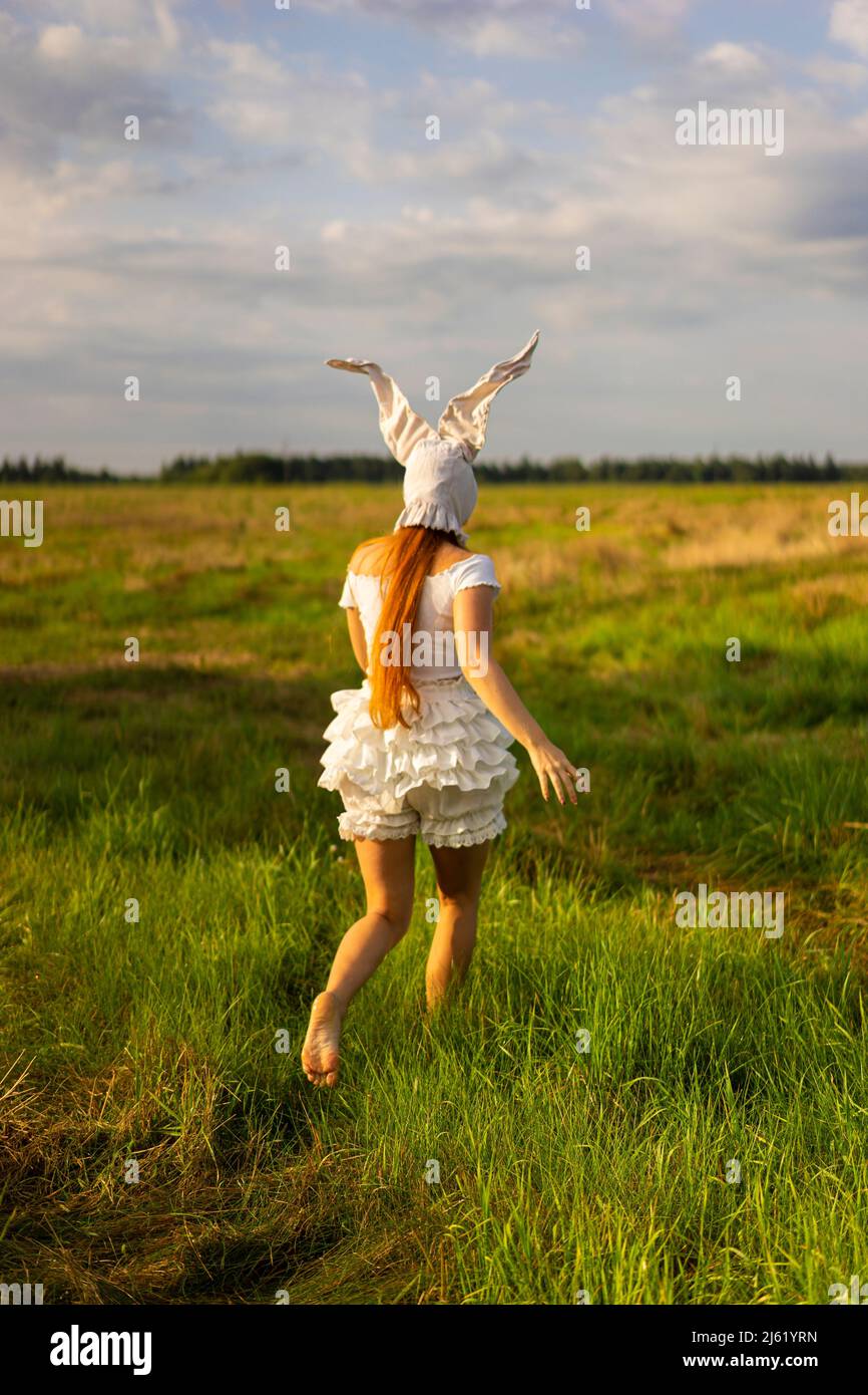 Junge Frau im Kaninchenkostüm, die auf dem Grasfeld läuft Stockfoto