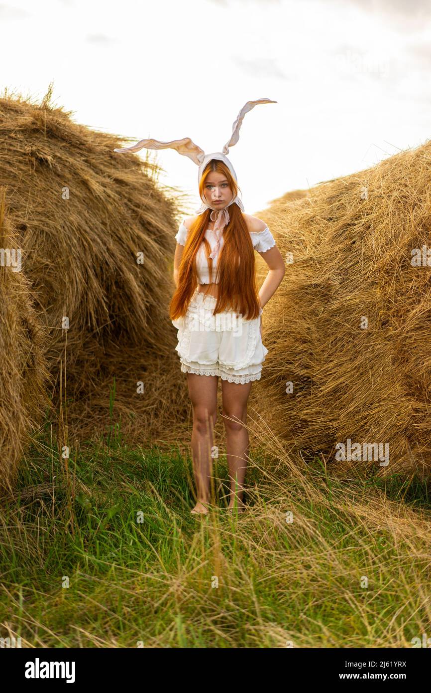 Junge Frau im Kaninchenkostüm, die inmitten von Heuballen steht Stockfoto