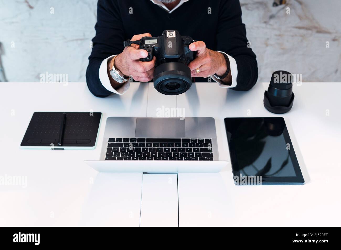 Freiberuflicher Mitarbeiter mit Kamera, der mit drahtlosen Technologien am Tisch sitzt Stockfoto