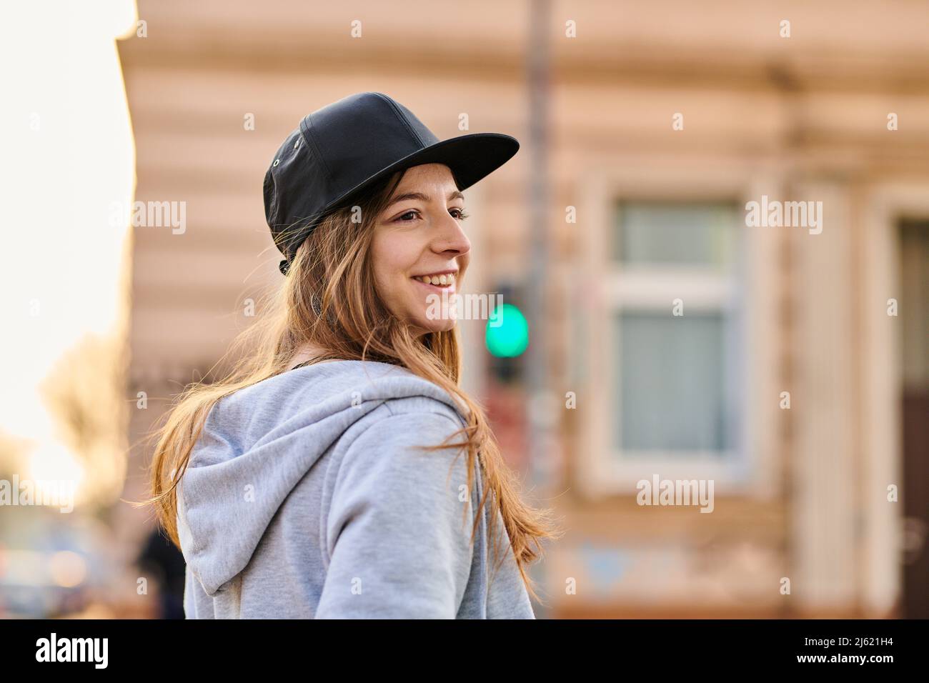 Lächelnde junge Frau mit Baseballmütze in der Stadt Stockfoto