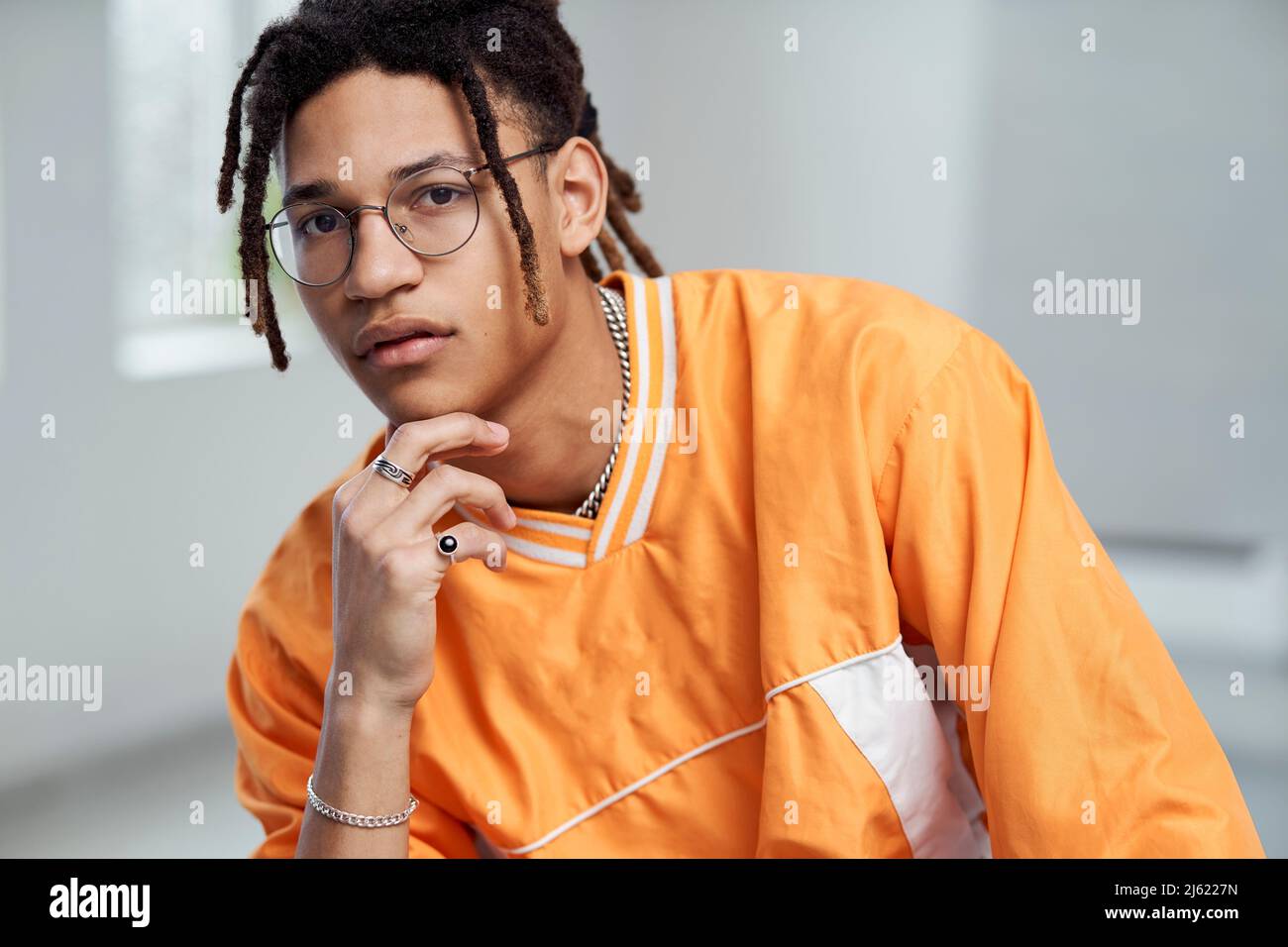 Junger Mann mit der Hand am Kinn und einer Brille Stockfoto