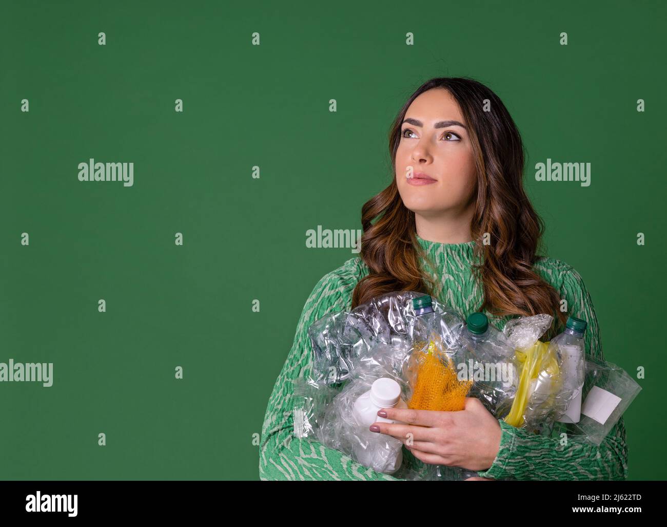 Junge Frau hält Plastikmüll vor grünem Hintergrund Stockfoto