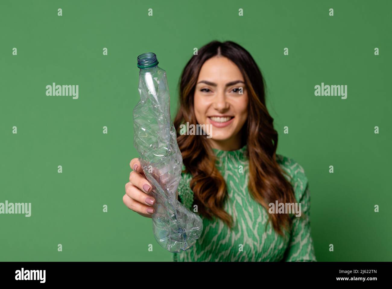 Lächelnde junge Frau zeigt Plastikflasche vor grünem Hintergrund Stockfoto