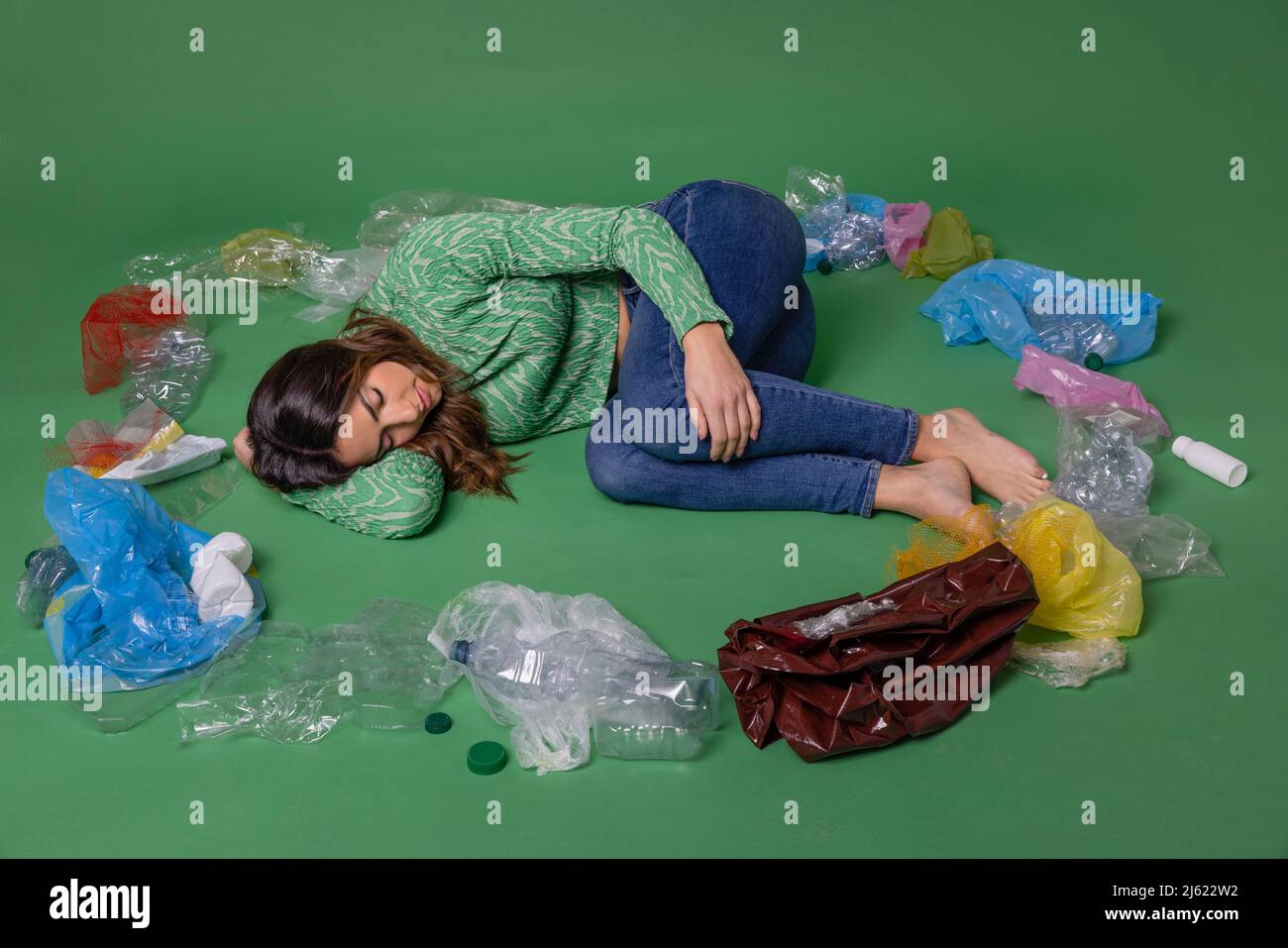 Frau liegt inmitten von Plastikmüll vor grünem Hintergrund Stockfoto
