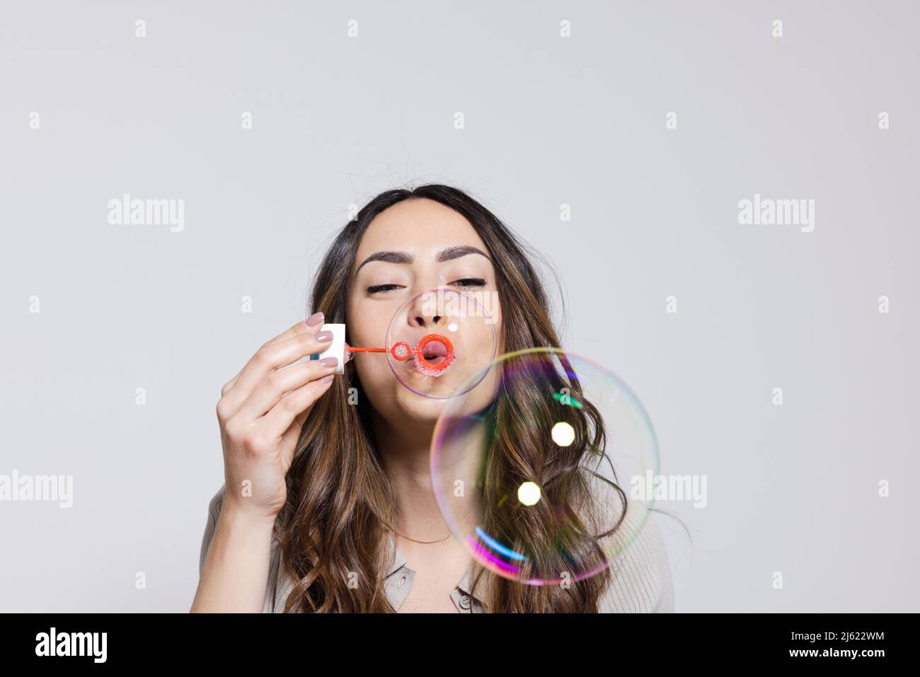 Junge Frau bläst Seifenblasen vor grauem Hintergrund Stockfoto