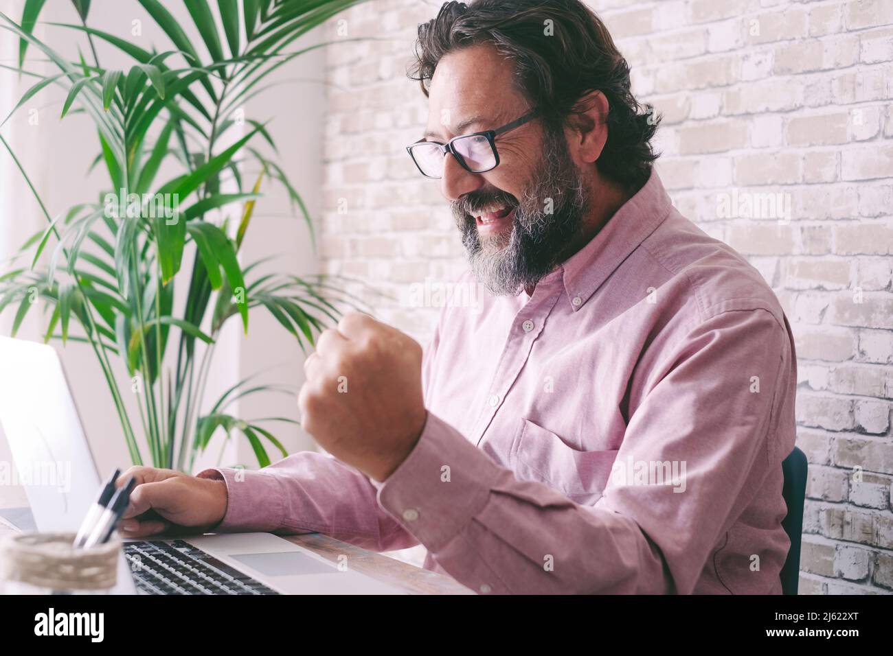 Fröhlicher Geschäftsmann, der zu Hause mit einem Laptop die Faust stikuliert Stockfoto