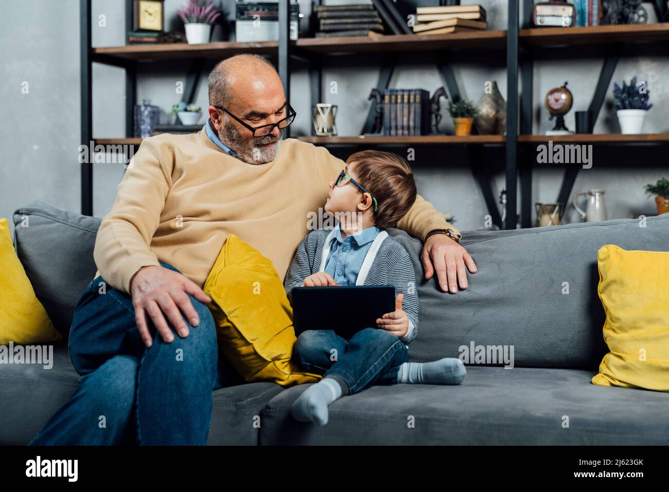 Junge mit Tablet-PC, der zu Hause beim Großvater auf dem Sofa sitzt Stockfoto