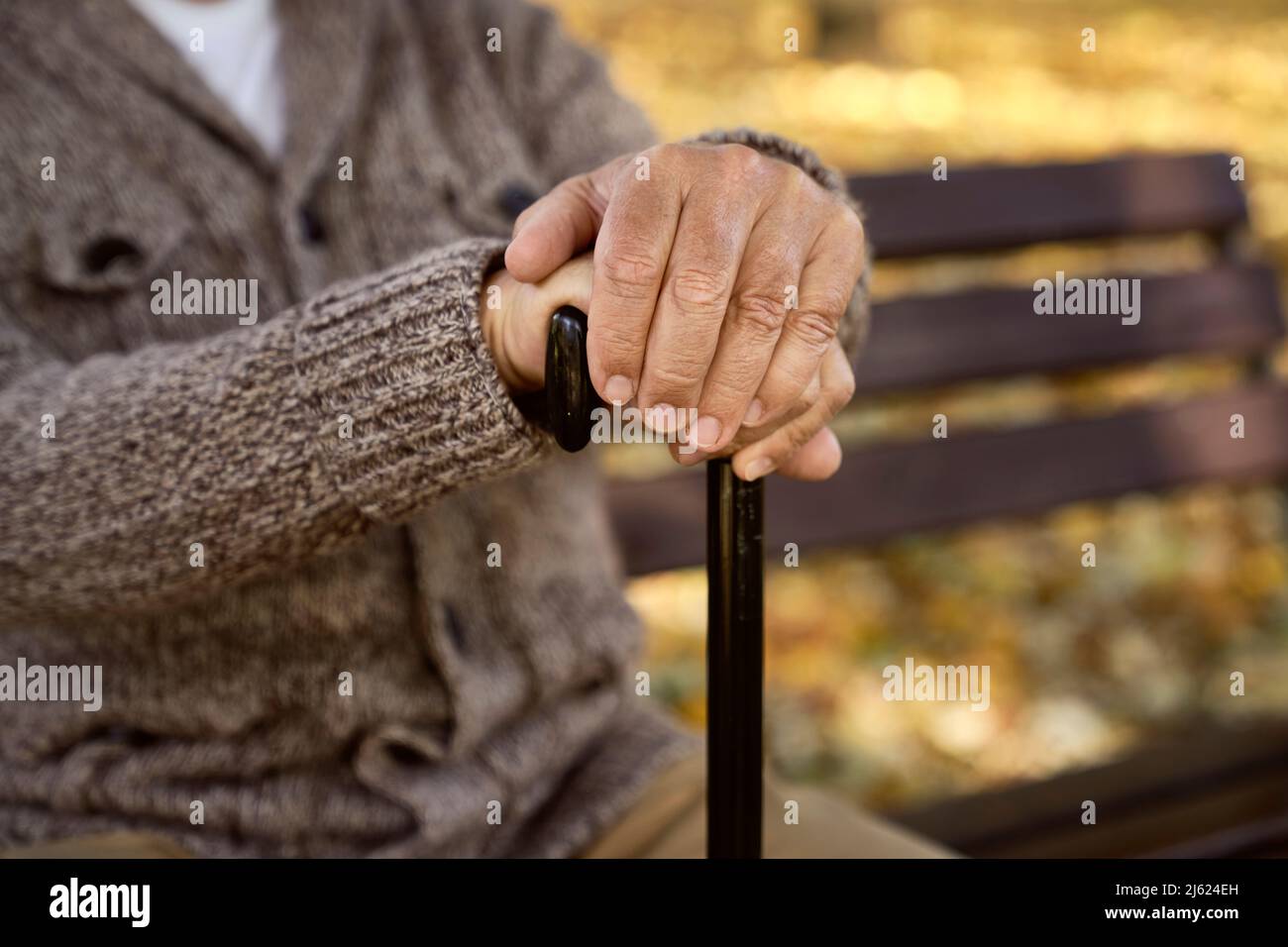 Älterer Mann, der mit Gehstock auf der Bank sitzt Stockfoto