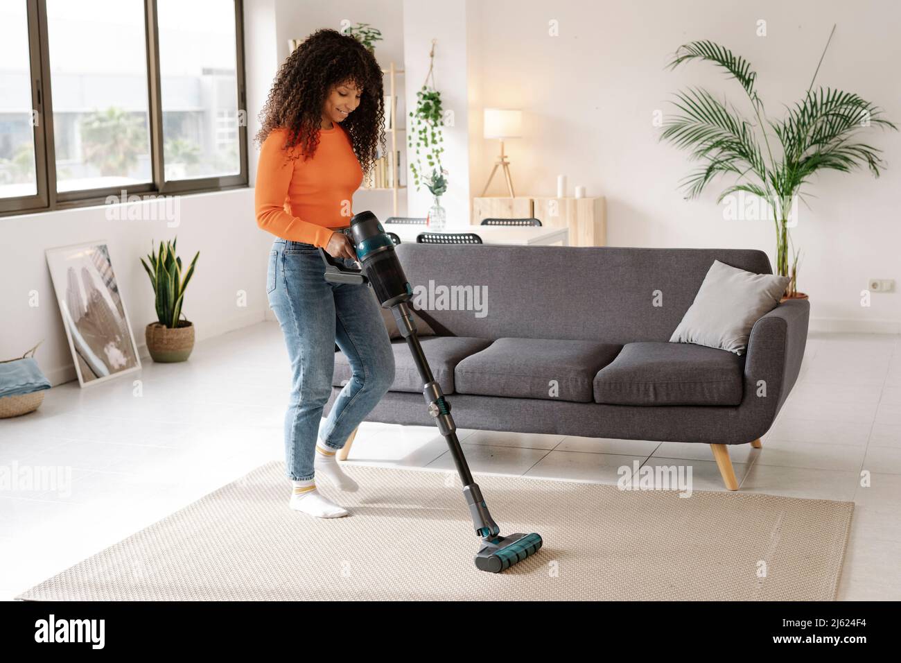 Junge Frau mit Staubsauger, die zu Hause Hausarbeit leistet Stockfoto