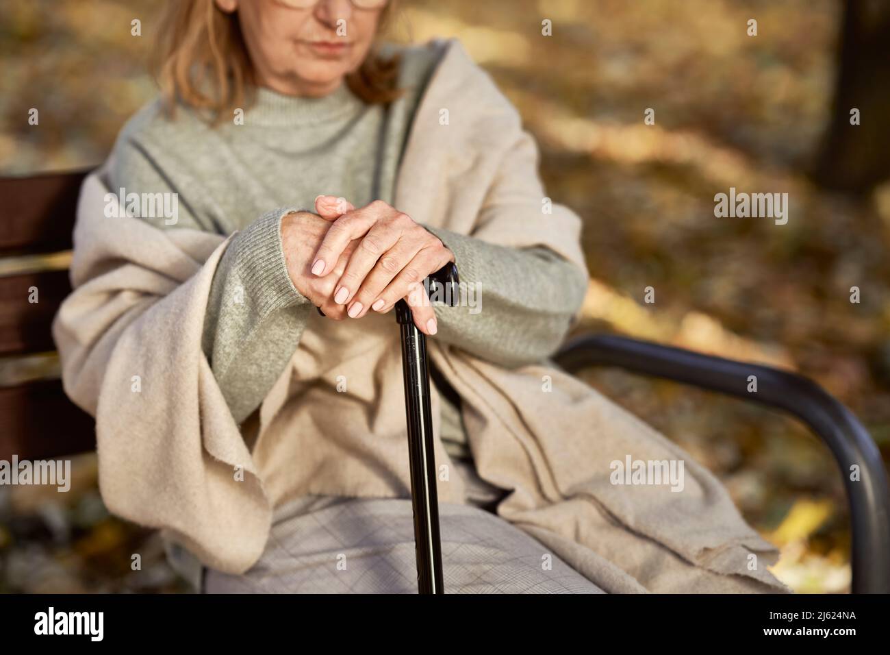 Ältere Frau mit Spazierstock sitzt auf der Bank im Park Stockfoto