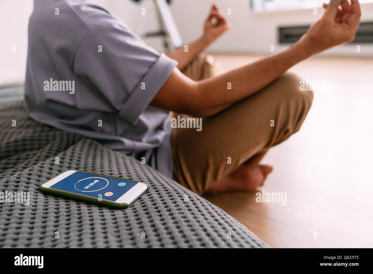Junger Mann, der zu Hause mit einem Smartphone und Timer meditiert Stockfoto