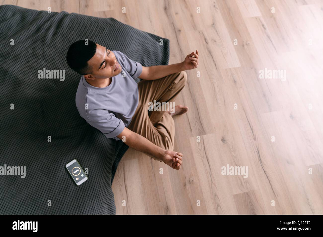 Junger Mann, der zu Hause Atemübungen mit dem Smartphone und Timer praktiziert Stockfoto