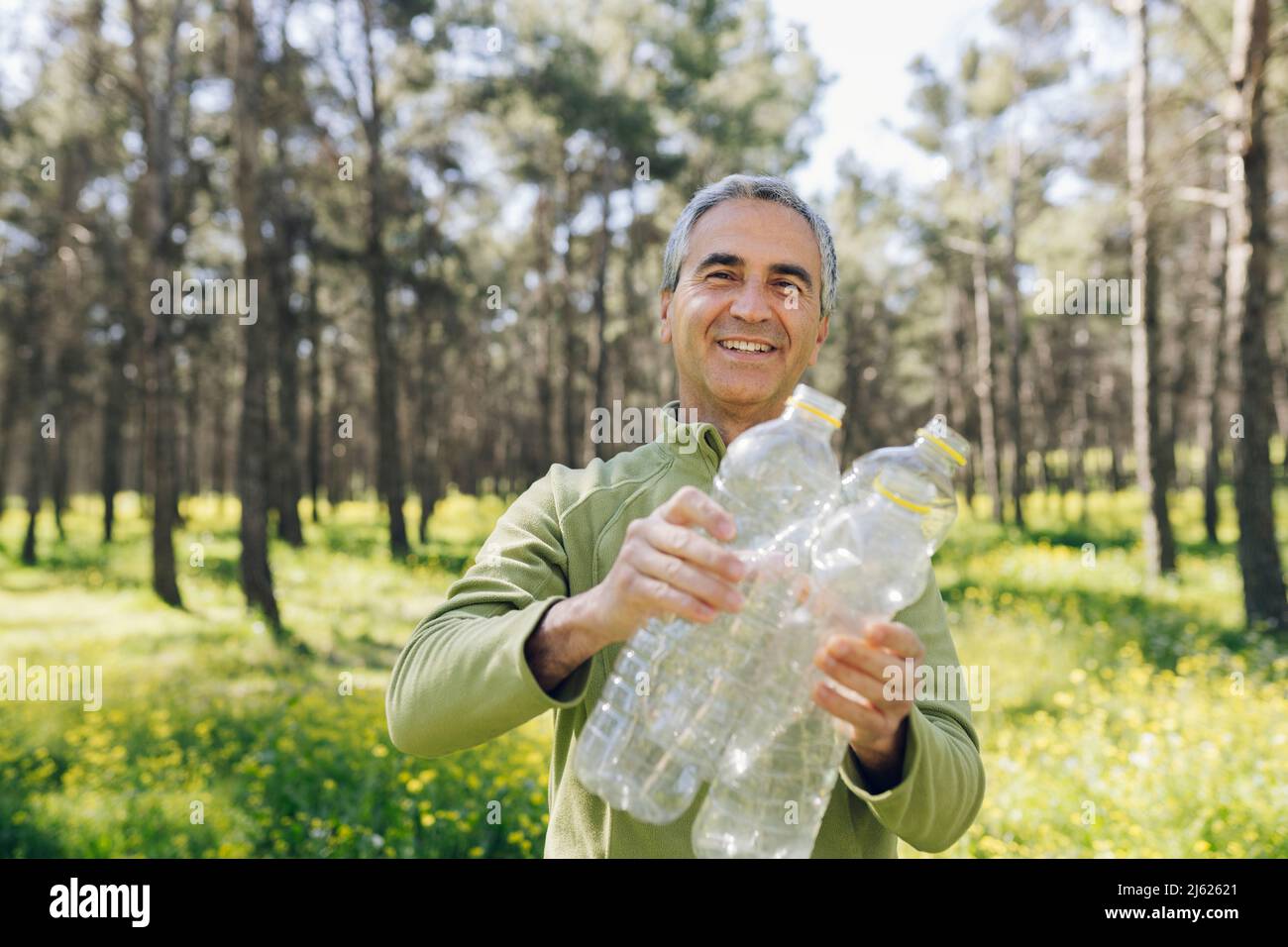 Glücklicher reifer Mann mit Plastikflaschen, die im Wald stehen Stockfoto