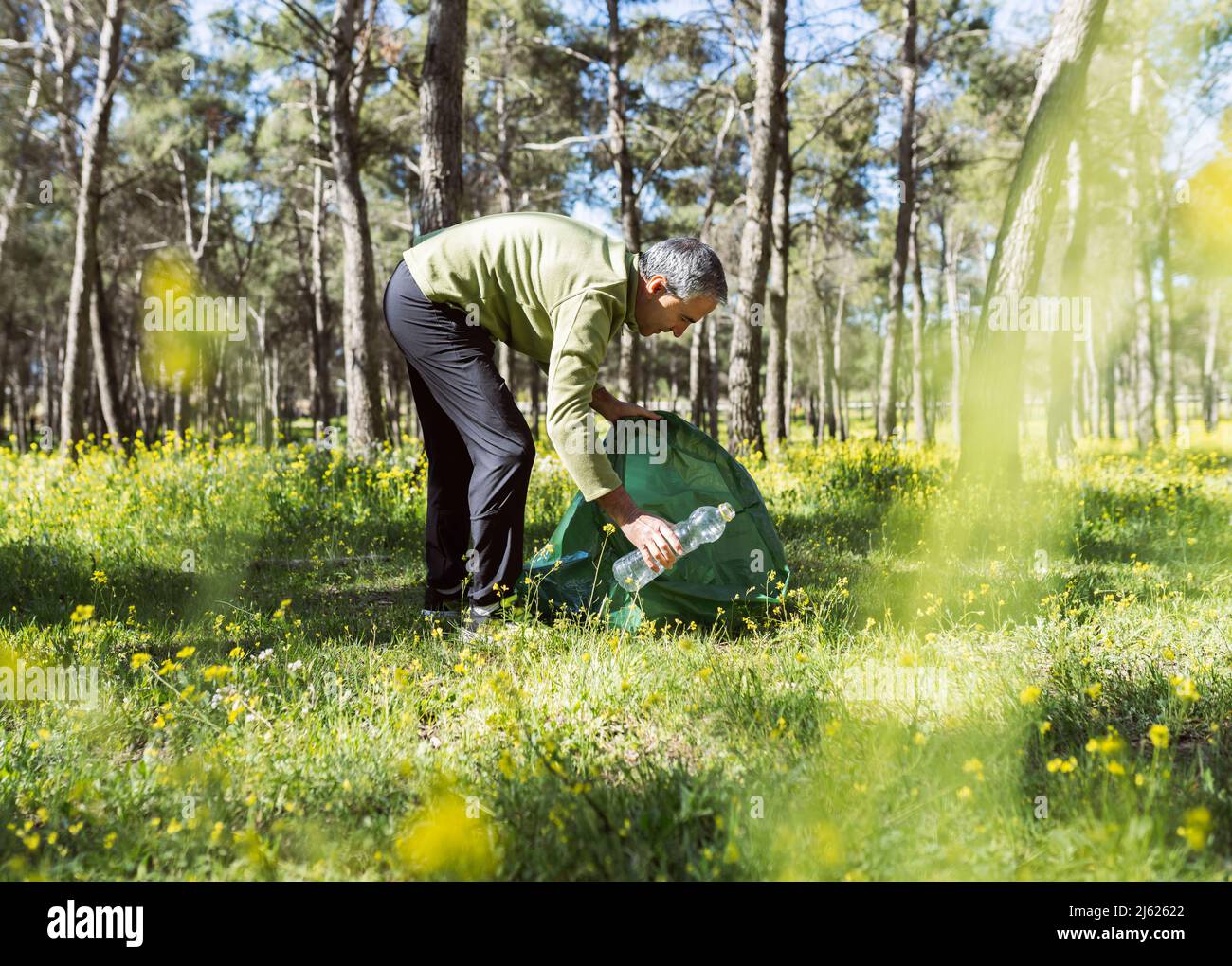 Mann sammelt Plastikflaschen im Wald an sonnigen Tag Stockfoto