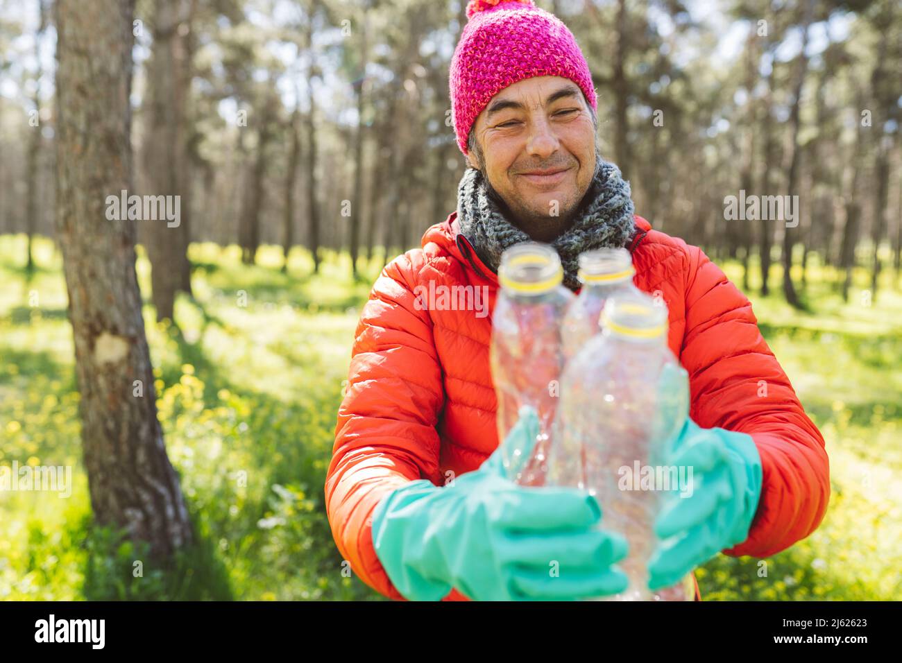 Lächelnder Mann mit Strickmütze, der Plastikflaschen im Wald hält Stockfoto