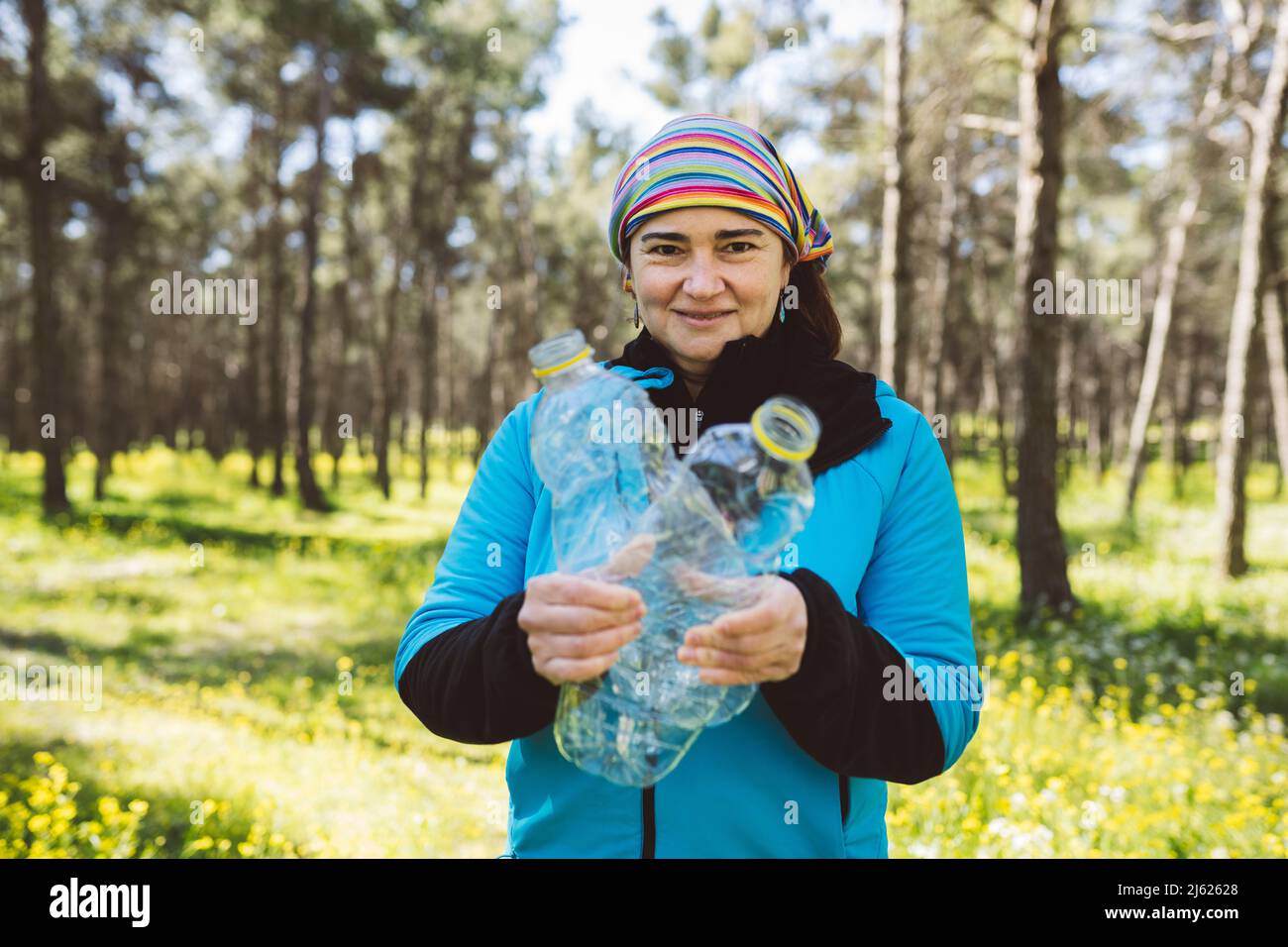 Lächelnde Frau mit Plastikflaschen, die im Wald stehen Stockfoto