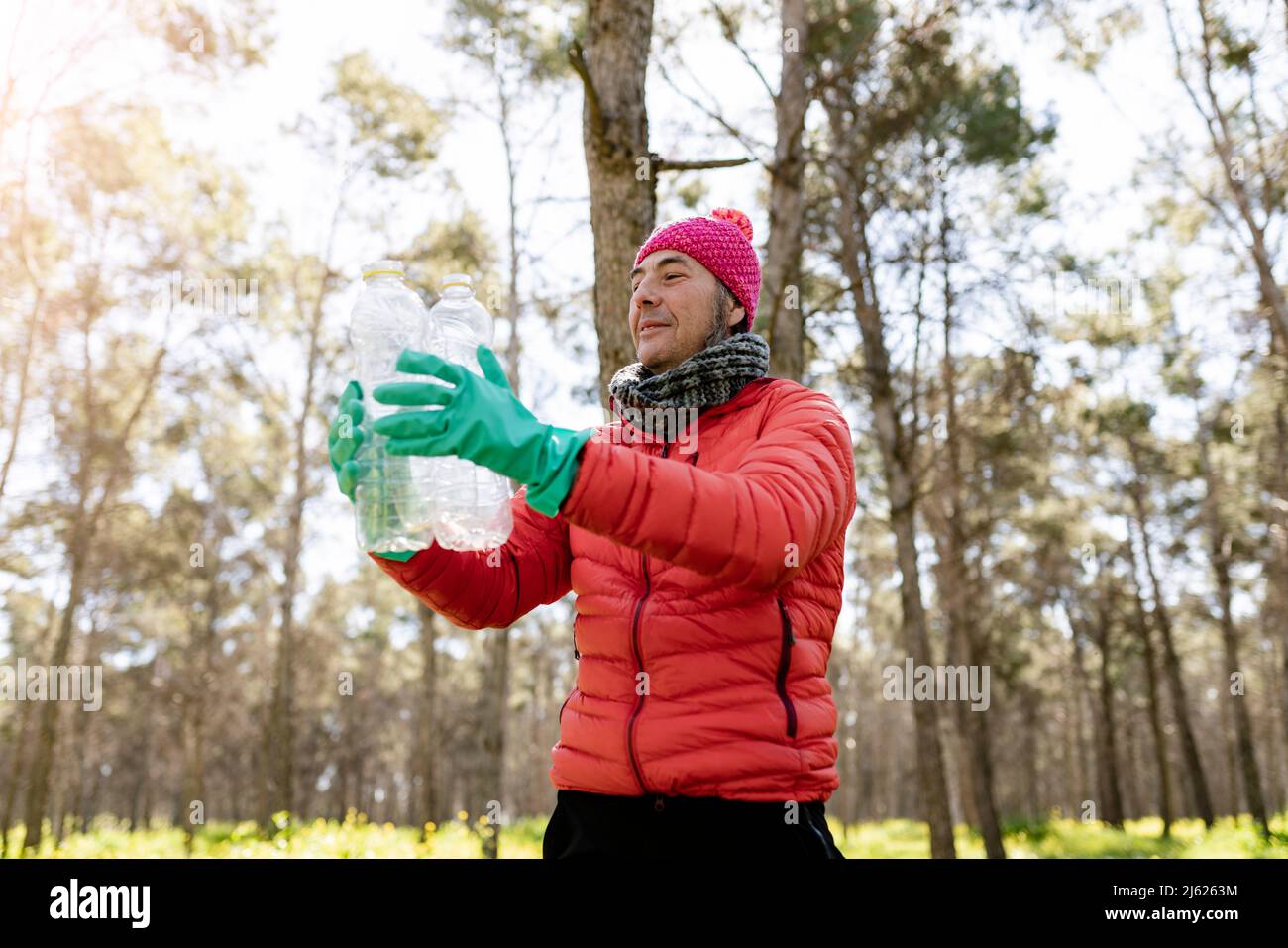 Mann mit Strickmütze, der Plastikflaschen im Wald hält Stockfoto