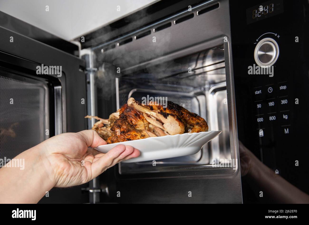 Ein Mann nimmt einen Teller gegrilltes Hähnchen aus der Mikrowelle. Das Konzept der Verwendung moderner Mikrowellenherde mit Grill und Konvektion Stockfoto