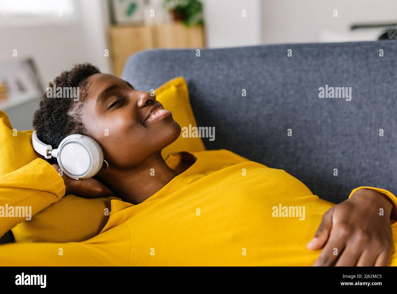 Afrikanerin, die sich zu Hause auf dem Sofa entspannt und Musik mit Kopfhörern hört Stockfoto
