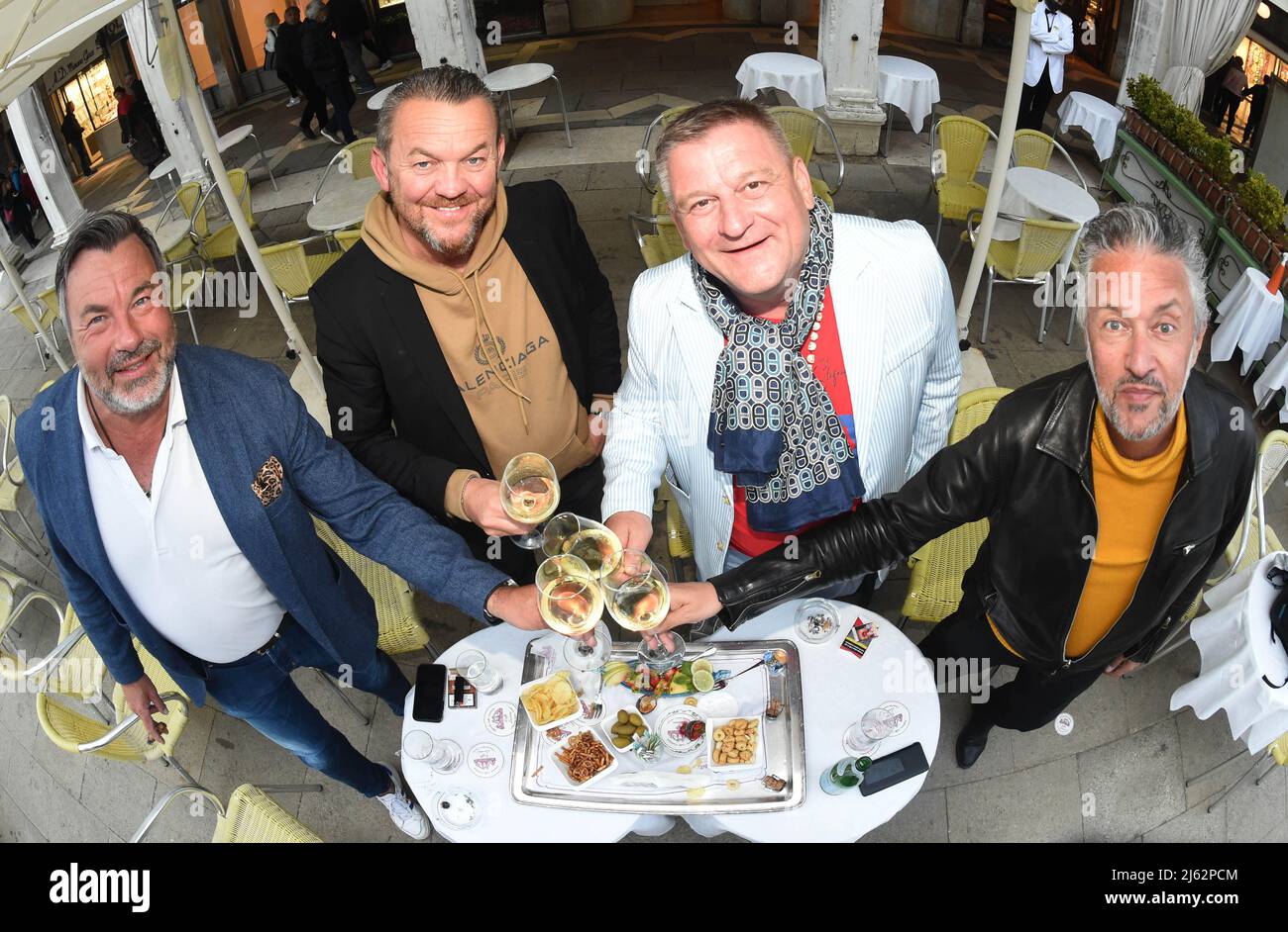 Venedig, Italien. 26. April 2022. Touristen Josef Klostermaier (l-r), Günther Abt, Stefan Grosse feiern mit Massimo Andreoli auf dem Markusplatz im Cafe Lavena, während die Kunstbiennale 59. in der Stadt stattfindet (aufgenommen mit Fischaugenobjektiv). Quelle: Felix Hörhager/dpa/Alamy Live News Stockfoto