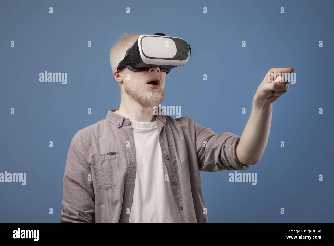 Virtuelle Welt in 3D Simulation. Aufgeregt Albino Kerl in vr Brille spielen und versuchen, etwas zu berühren, blauer Hintergrund Stockfoto