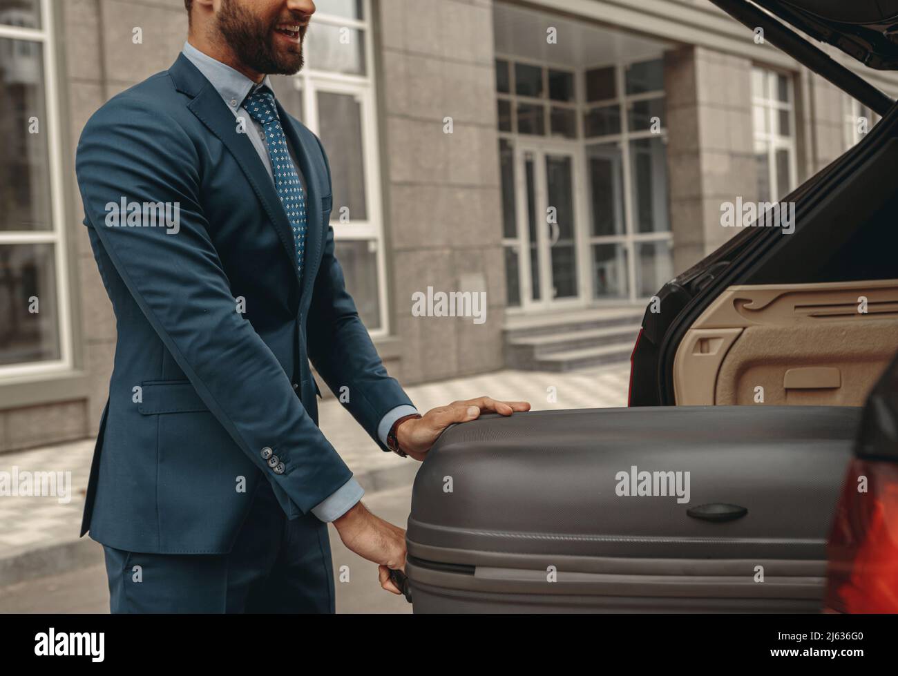 Lächelnder eleganter Rüde im Anzug geht mit dem Business Car auf die Geschäftsreise Stockfoto