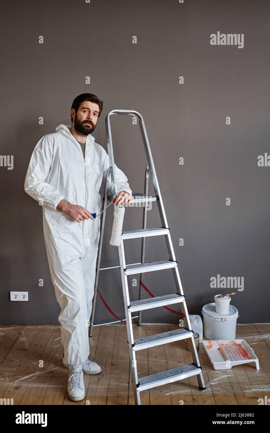 Vertikale Aufnahme eines kaukasischen Mannes mit Schutzkleidung, der in seiner Wohnung Renovierungsarbeiten durchgeführt hat und dabei die Kamera ansah Stockfoto